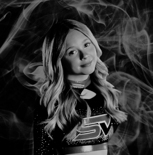 Blonde cheerleader in uniform, smiling. Black and white photo with smoky background.