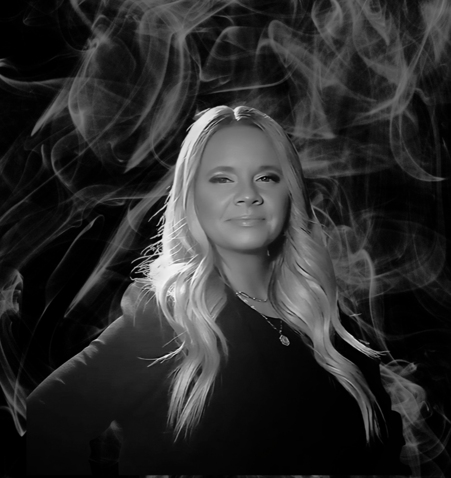 Woman with blonde hair, smiling, in front of a dark smoky background.