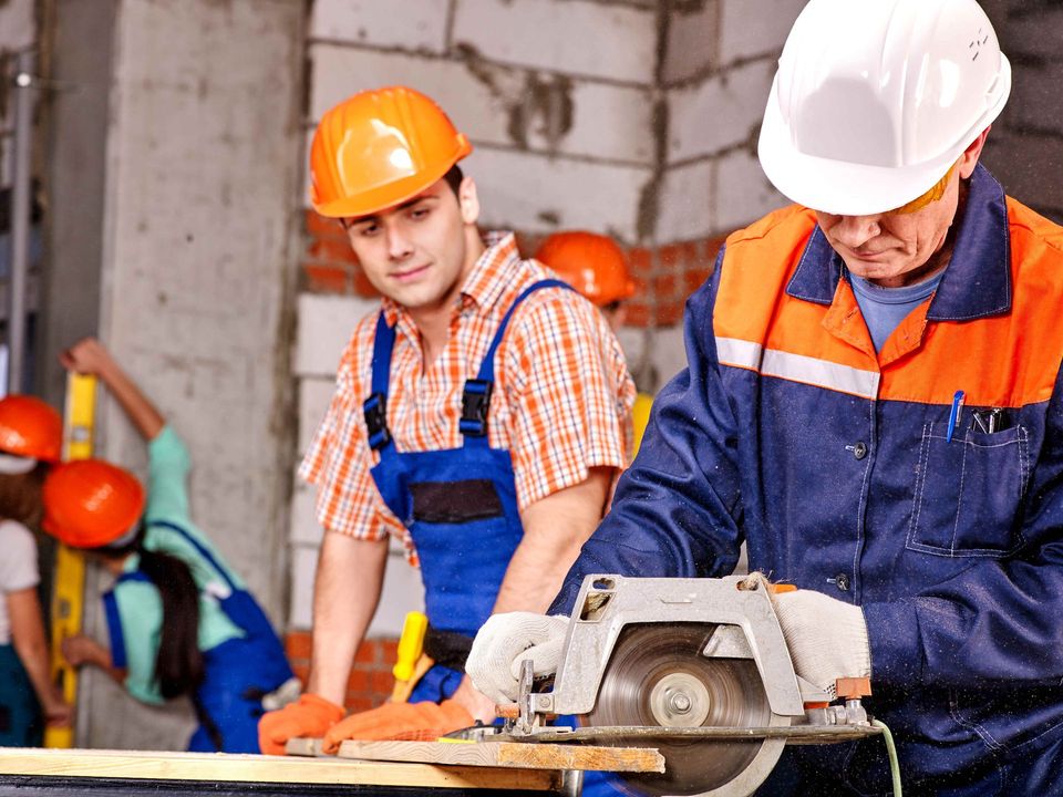 two construction workers are using a circular saw to cut a piece of wood