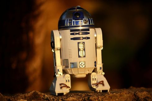 A toy r2d2 from star wars is sitting on a rock.