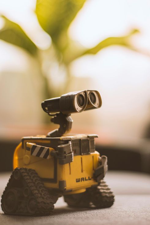 A toy wall e robot is sitting on a table in front of a plant.