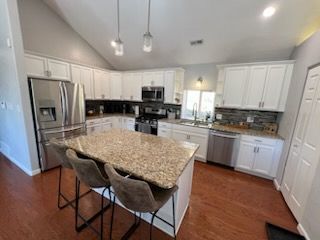 A kitchen with white cabinets , granite counter tops , stainless steel appliances and a large island.