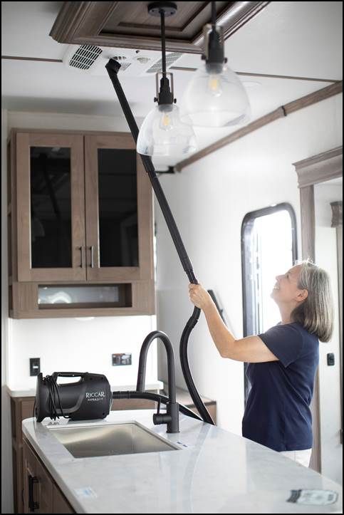 A woman is using a vacuum cleaner to clean the ceiling in a kitchen. - Capistrano Sewing Machine - Capistrano, CA