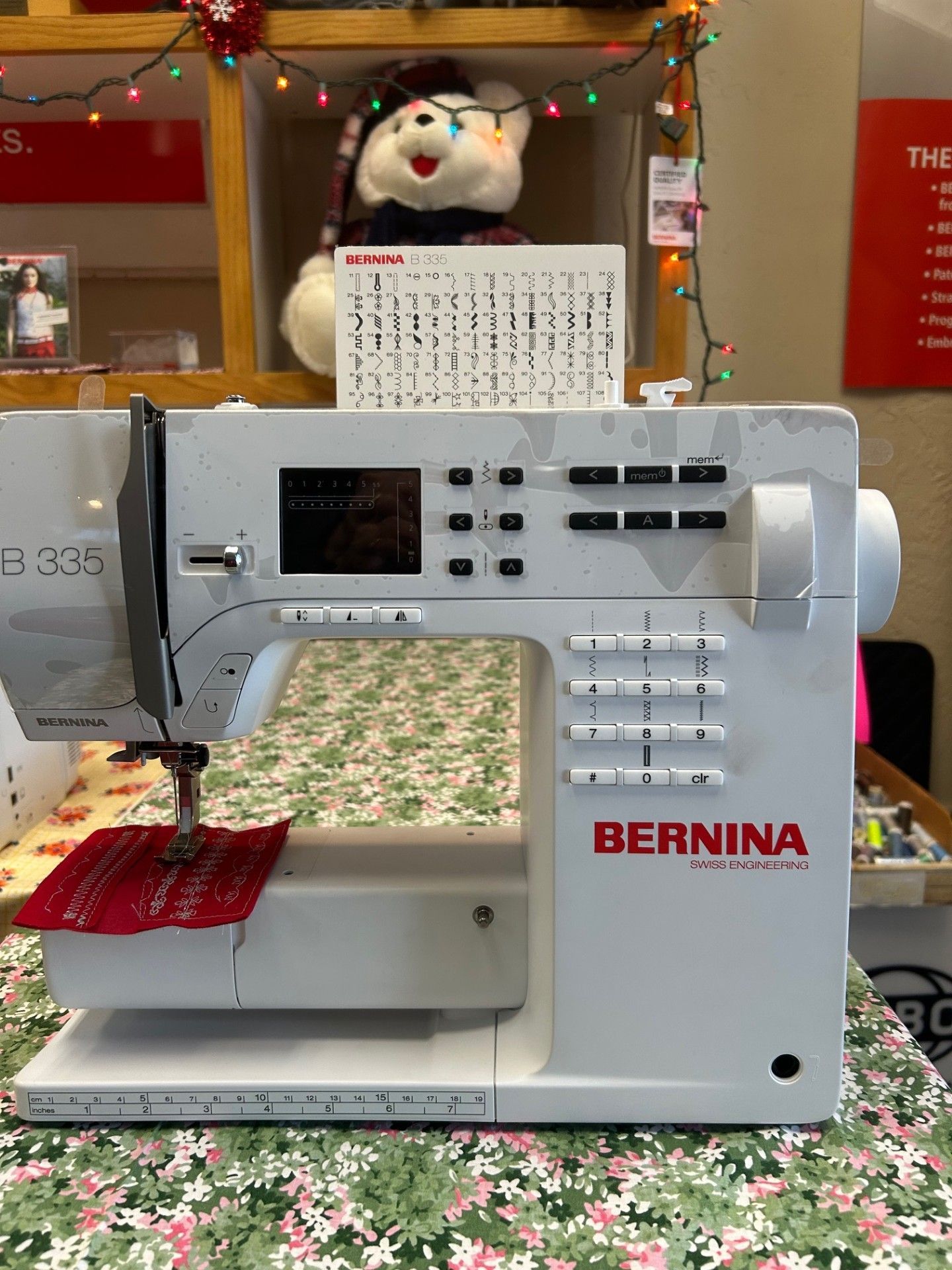 Bernina sewing machine, white and gray, sewing red fabric on floral table.