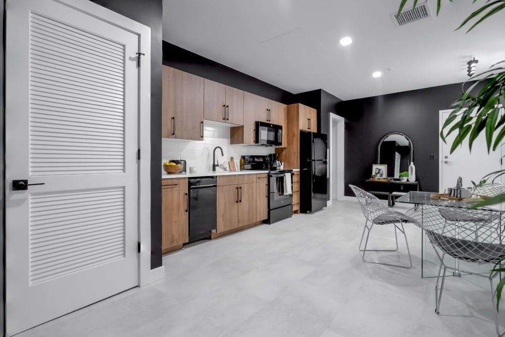 A kitchen with wooden cabinets and black appliances and a dining room with a table and chairs.