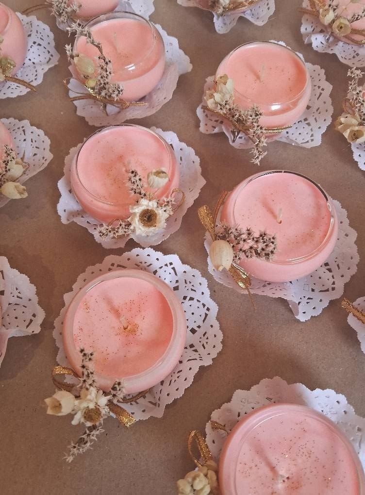 Velas rosas en tarros de cristal, decoradas con flores secas, sobre blondas blancas.
