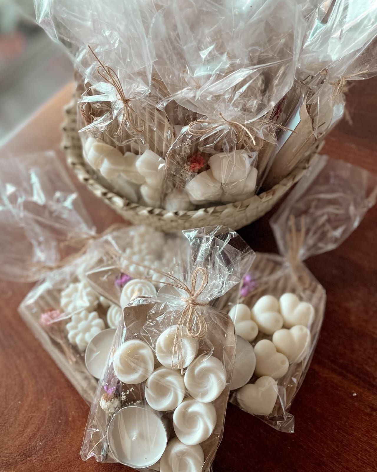 Cera blanca derretida en bolsas de celofán transparente atadas con cordel, dispuestas en una cesta.