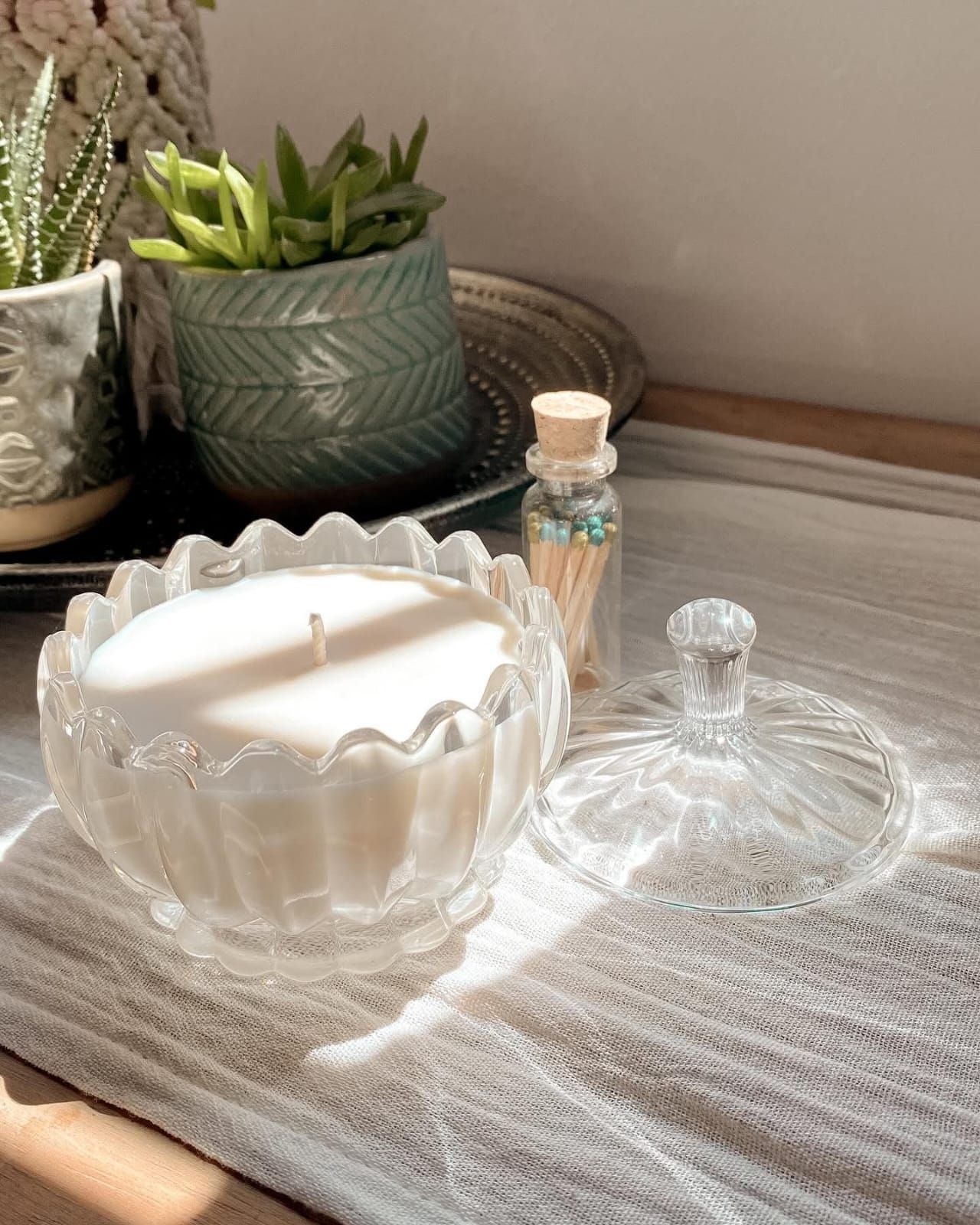 Una vela en un plato de vidrio transparente con borde ondulado y tapa