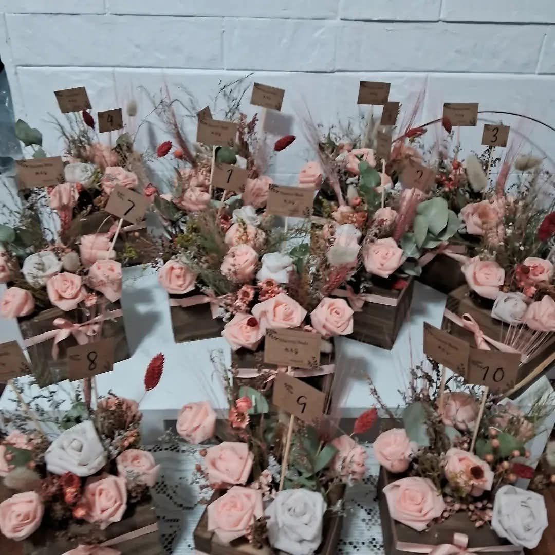 Centros de mesa florales con rosas rosas, cajas de madera y números de mesa en tarjetas.