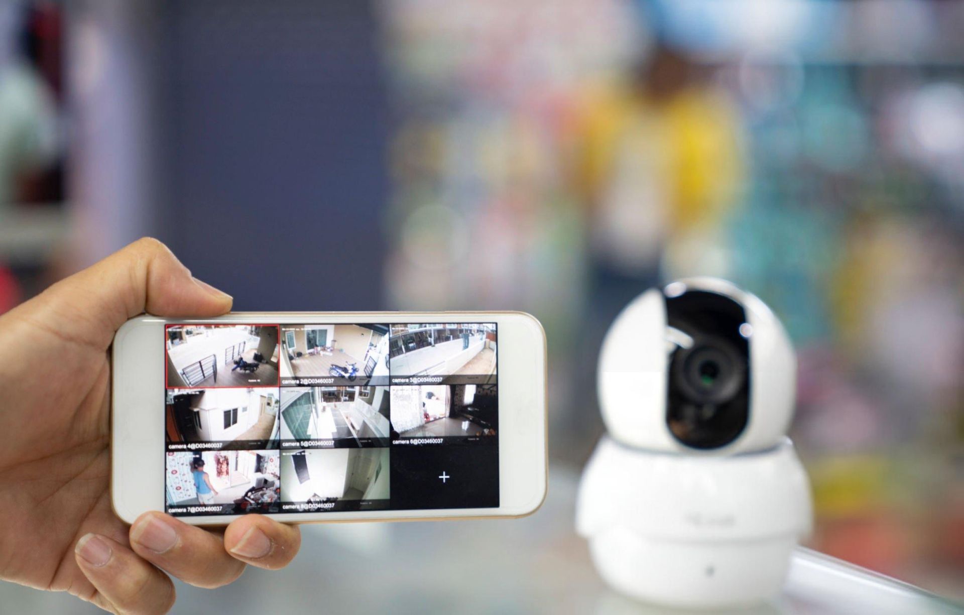 A person's hand holding a mobile phone with CCTV camera footage on the screen.