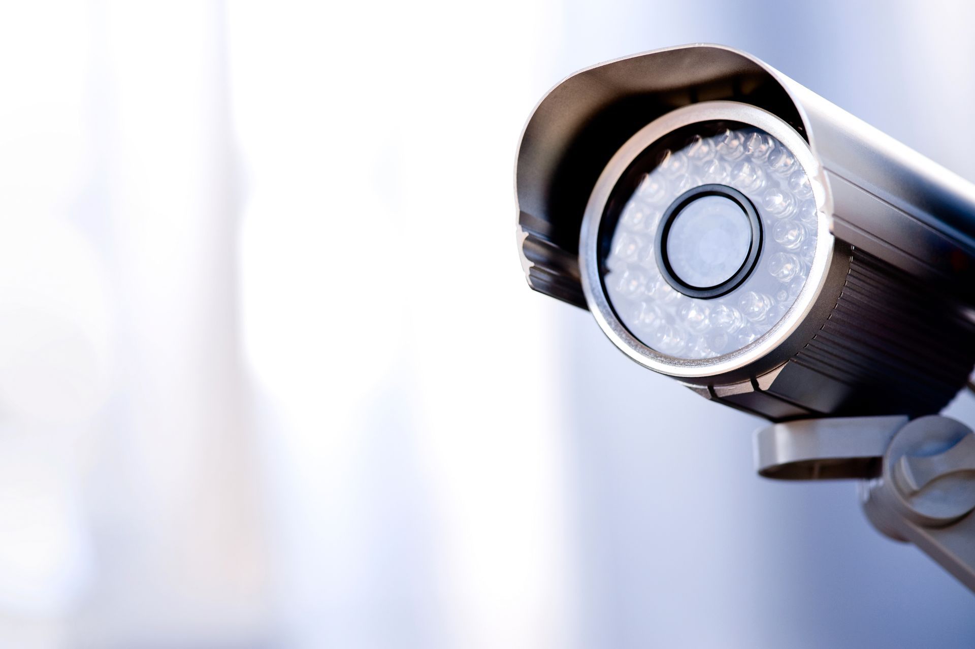 Close-up of a security camera’s lens, with a blurry and gray background.