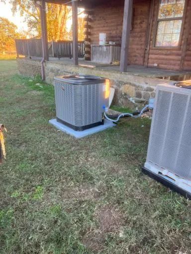 Two outdoor HVAC units beside a wooden house at sunset