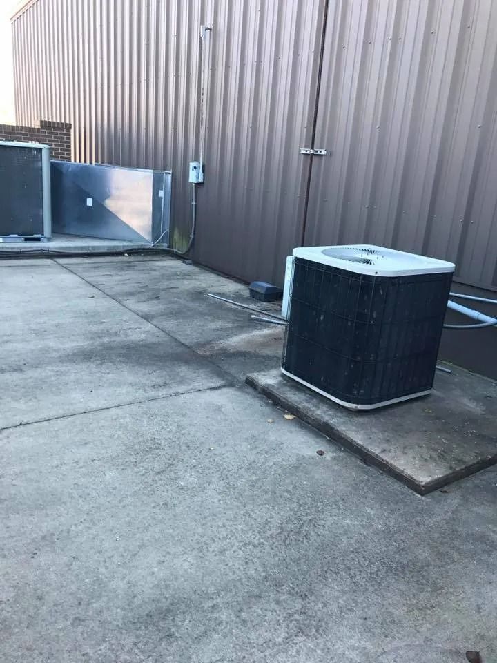 Outdoor utility area with concrete pavement, metal wall, and two HVAC units near a gate.
