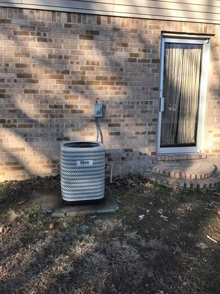Outdoor HVAC unit beside a brick house wall and back door in a shaded yard
