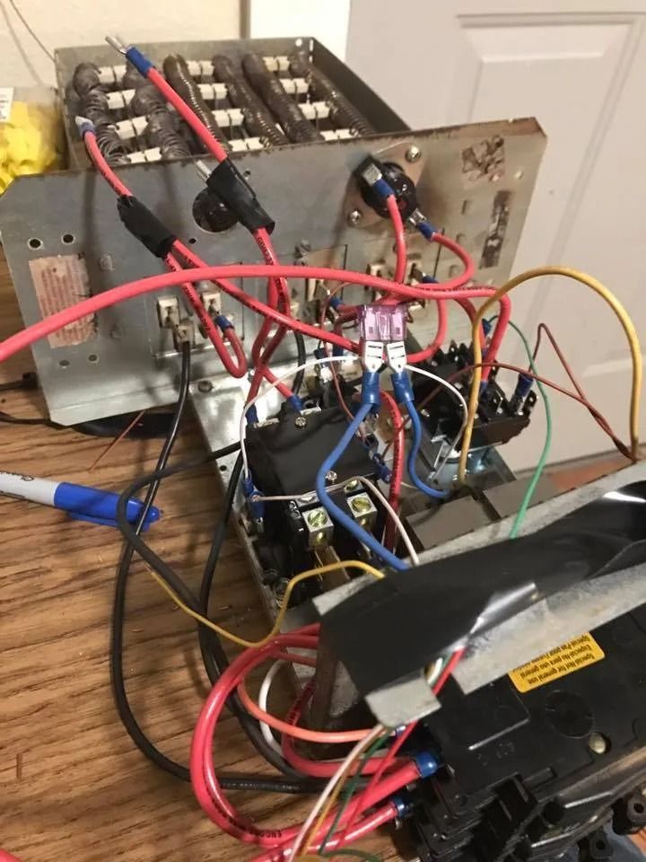 Messy electronics wiring setup with red, blue, and yellow cables on a wooden table and metal frame