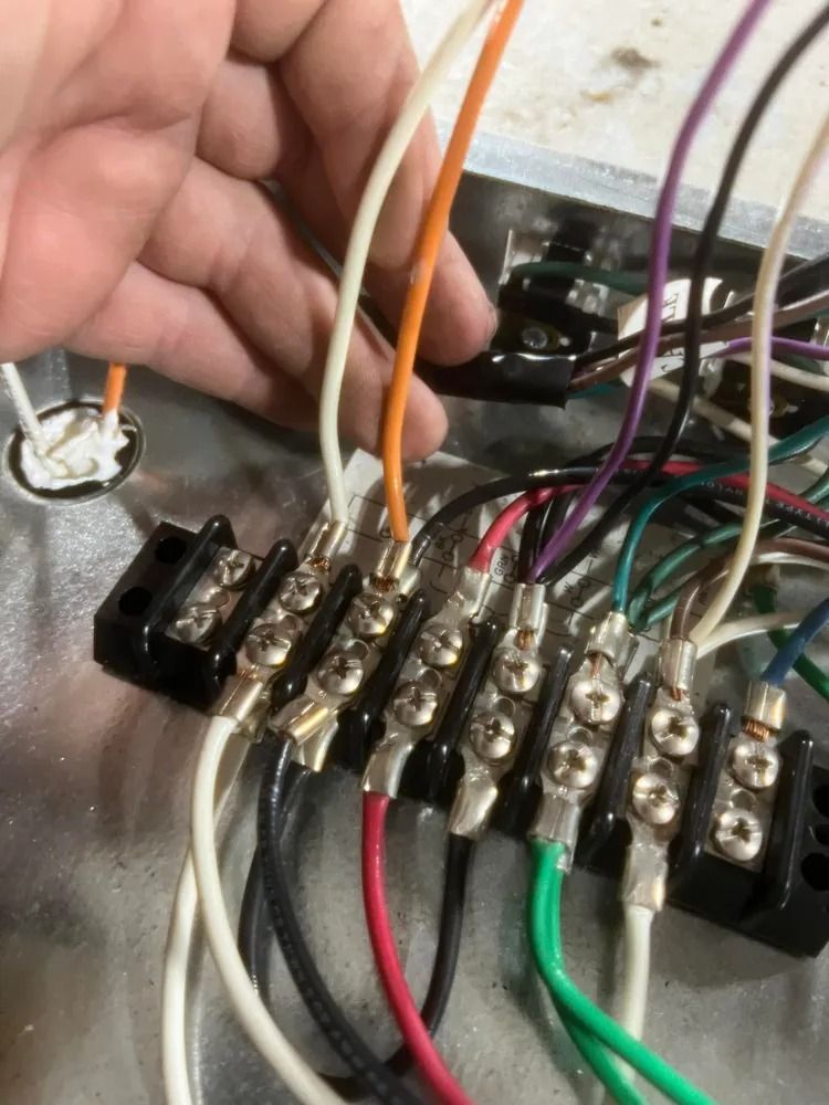 Hand wiring electrical terminals on a black terminal block with colored wires attached