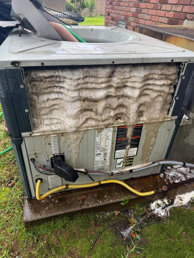 Outdoor HVAC unit with dirty, water-stained coils and exposed wiring by a brick wall.