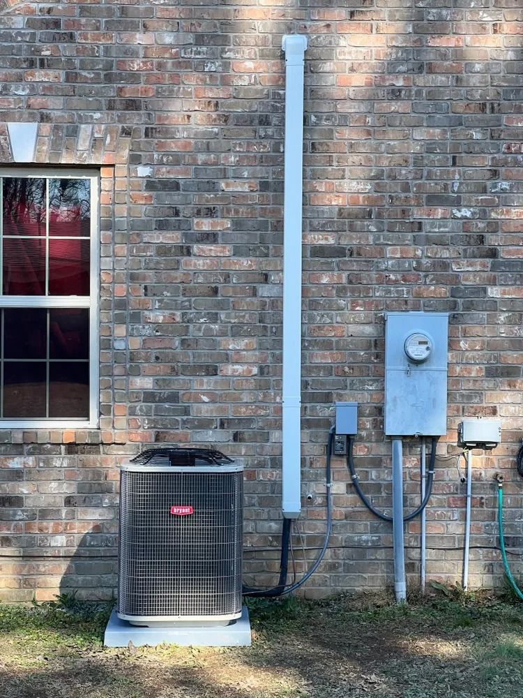 Outdoor HVAC unit and electrical equipment mounted on a brick building wall next to a window.