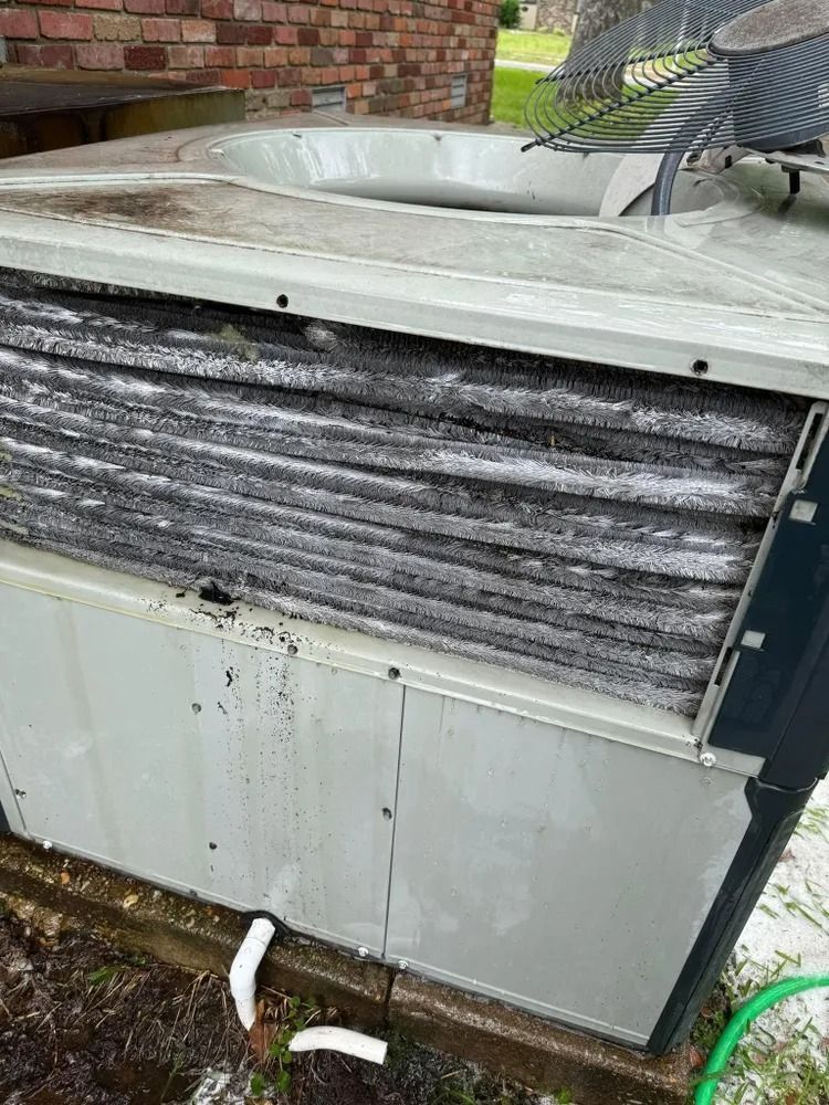 Damaged outdoor HVAC unit with bent top and dirty, corroded fins beside a brick wall