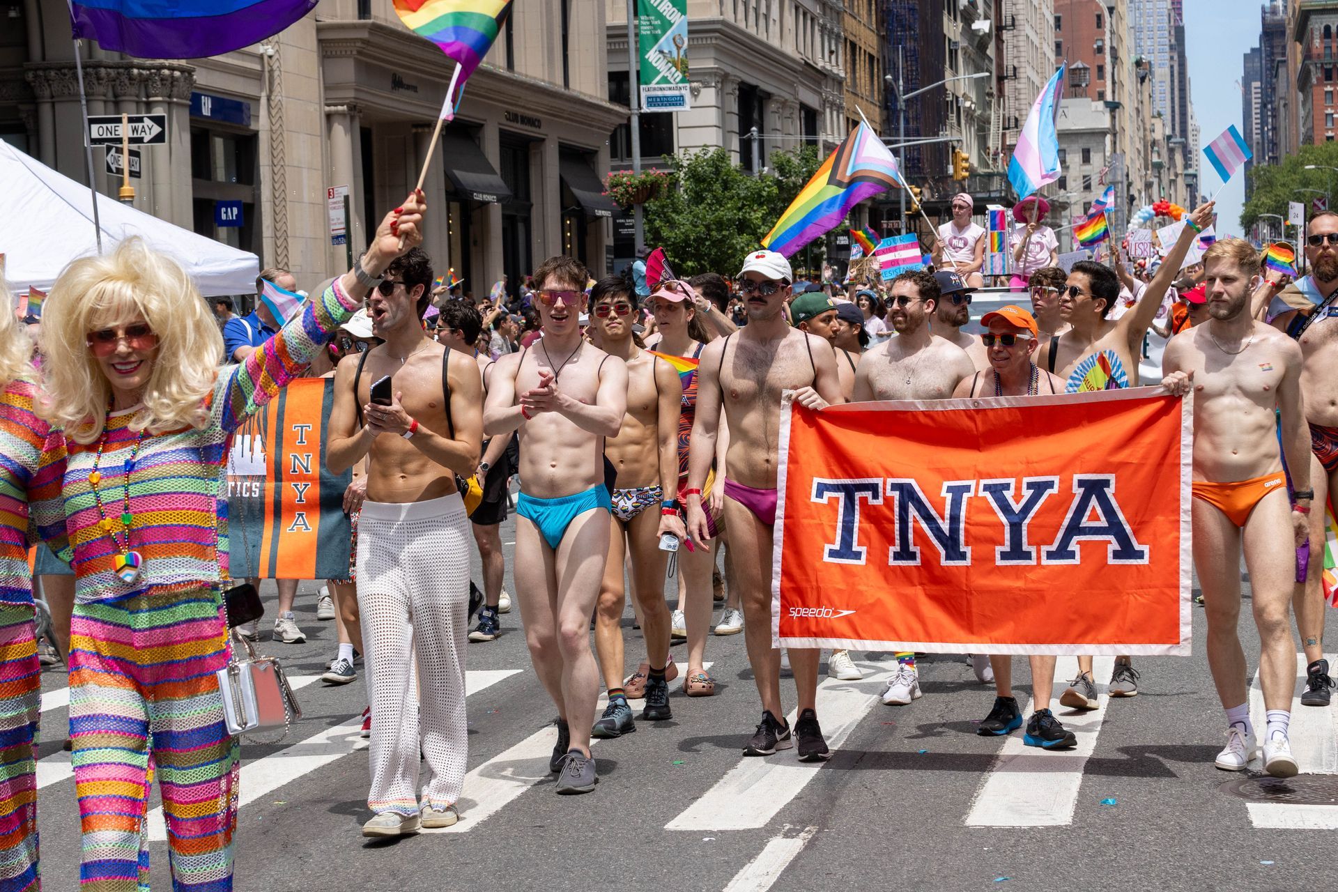 Pride parade: People marching, some shirtless, carrying flags and a banner reading 