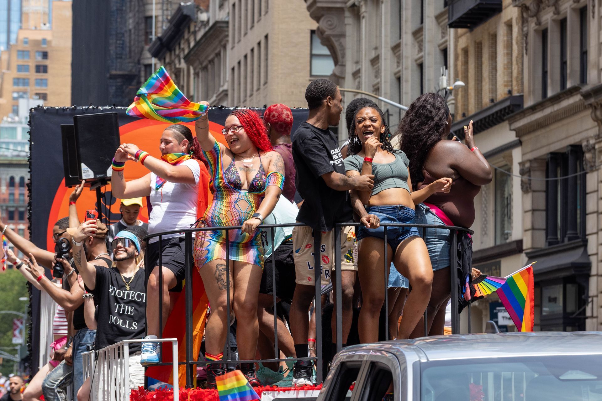 Pride parade float with diverse people waving rainbow flags, smiling in NYC.