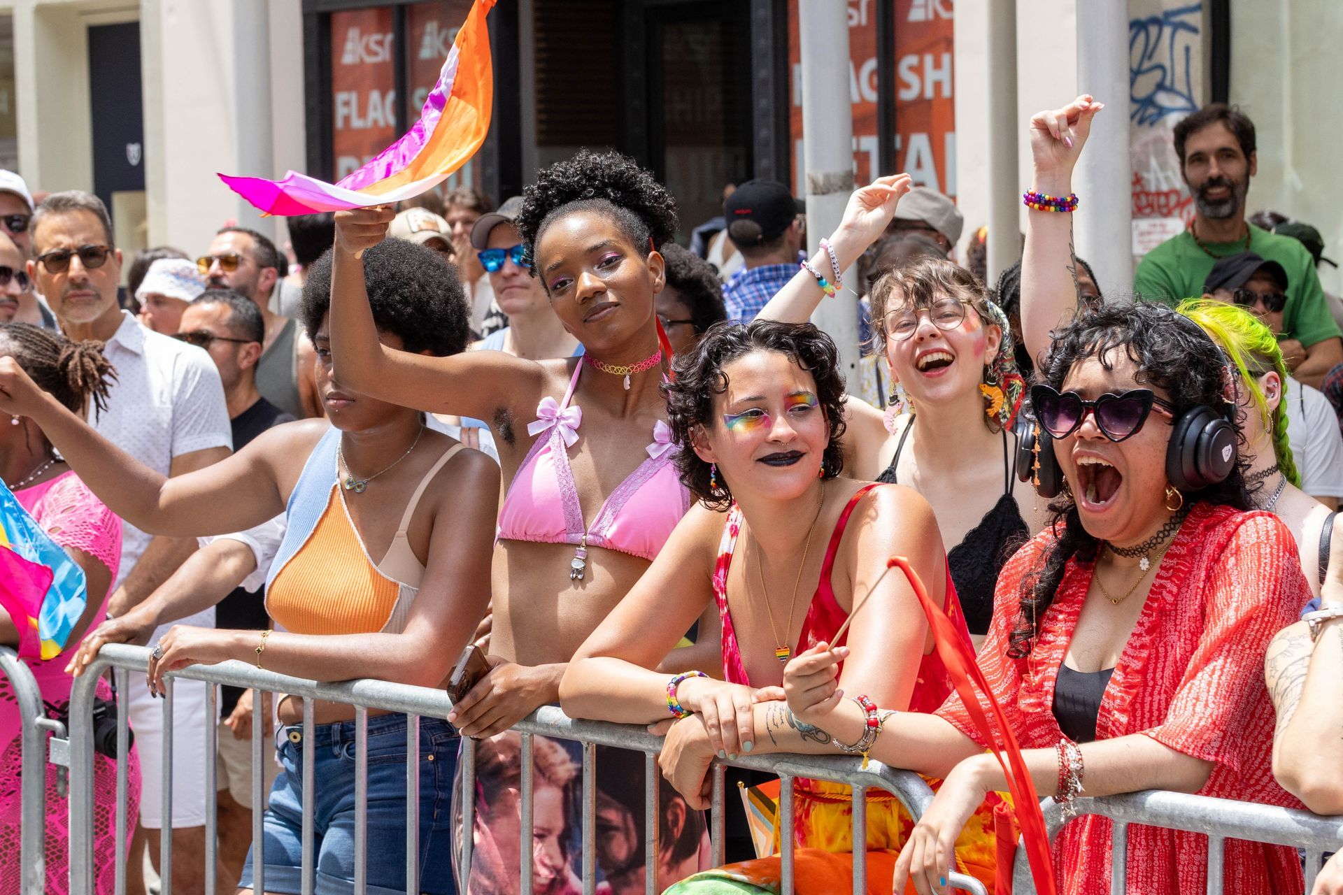 People cheering at a Pride parade, some with colorful accessories and expressions. Street setting.