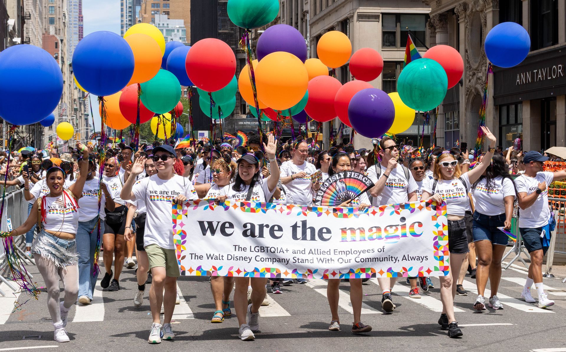 People in a Pride parade holding balloons and a banner that reads 