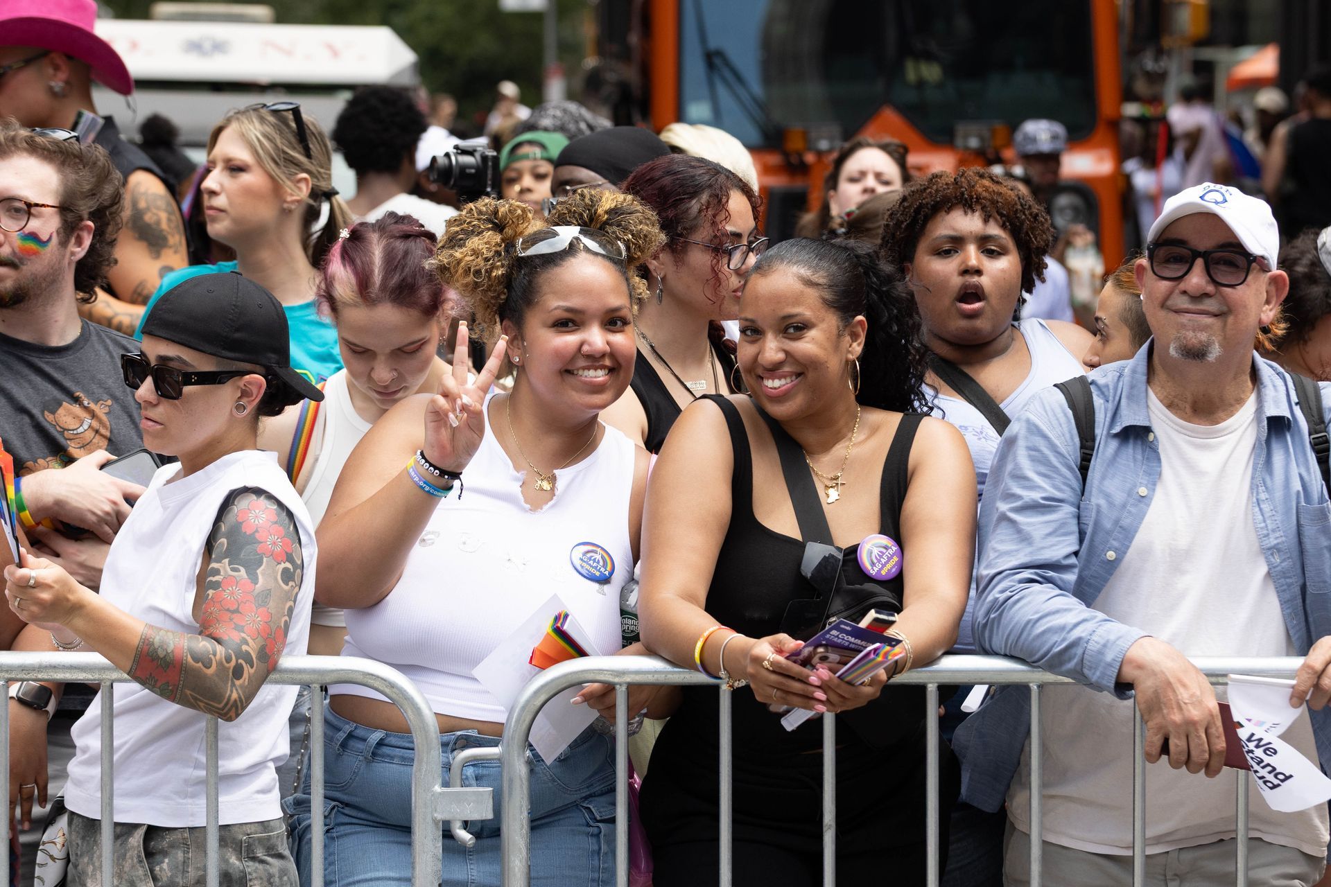 People at a Pride event behind a barrier, smiling, with some holding flags.
