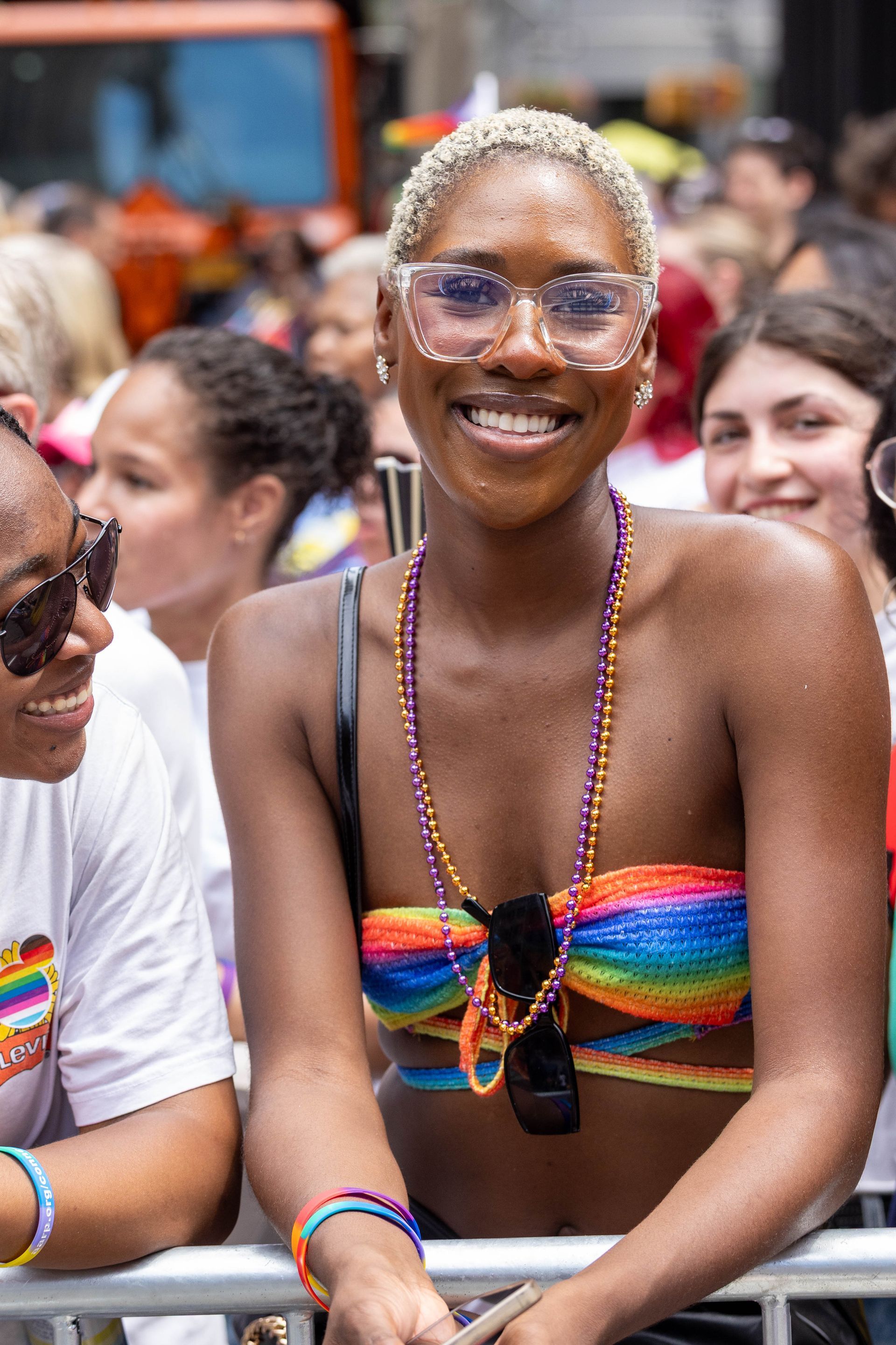 Smiling person at Pride parade wearing rainbow top and glasses.