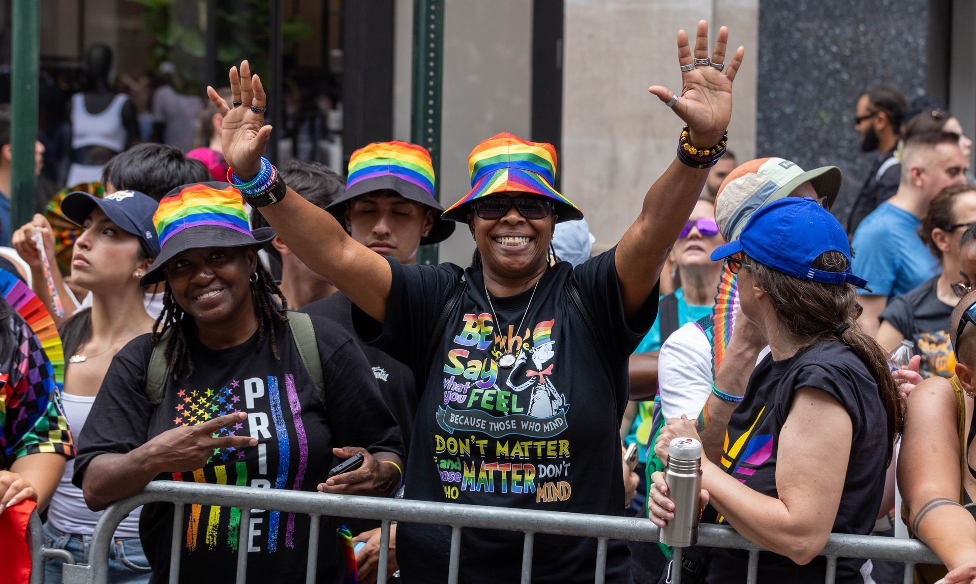 People at Pride parade, wearing rainbow hats, waving, smiling. New York City.
