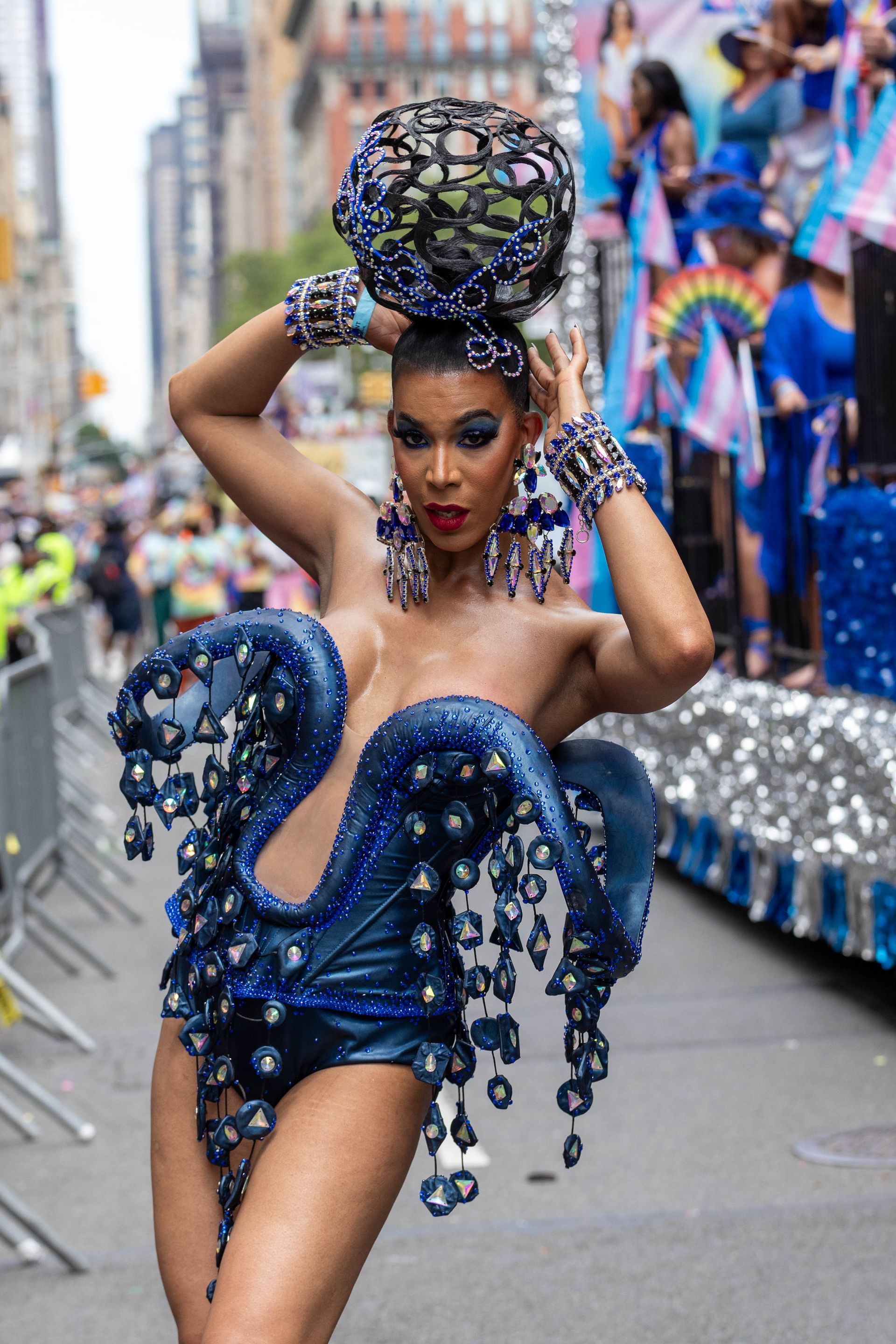 A drag queen in a blue octopus-themed costume at a pride parade, striking a pose.