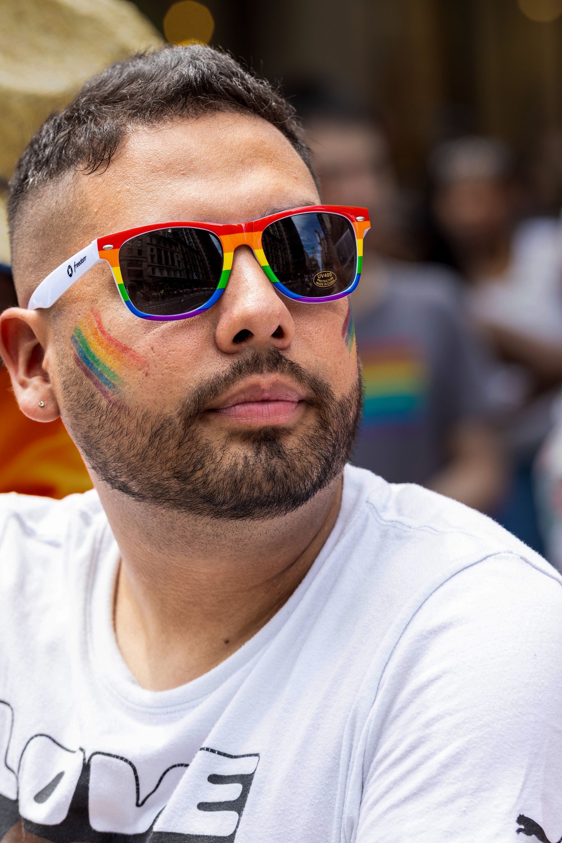 Man wearing rainbow sunglasses and face paint at Pride event.