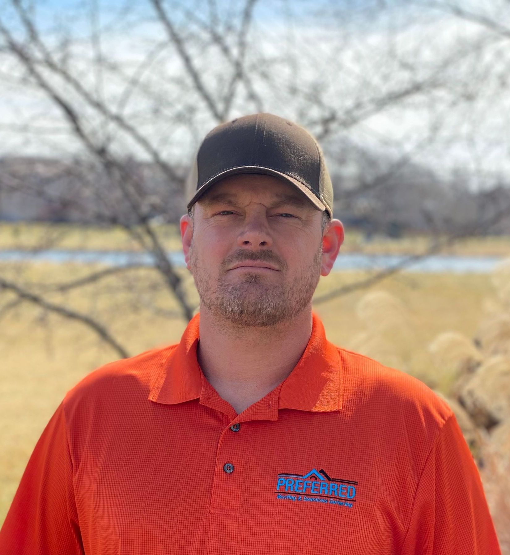 A man wearing an orange shirt and a black hat is standing in a field.