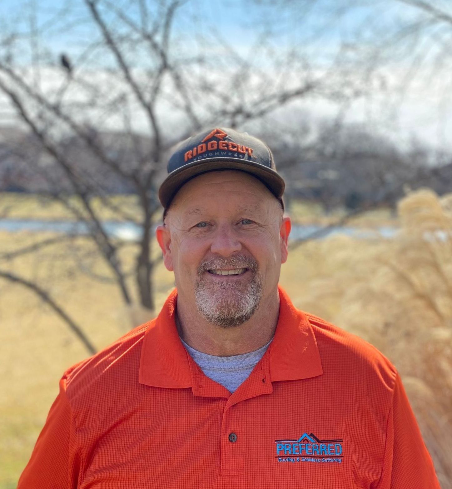 A man wearing an orange shirt and a hat is smiling for the camera.