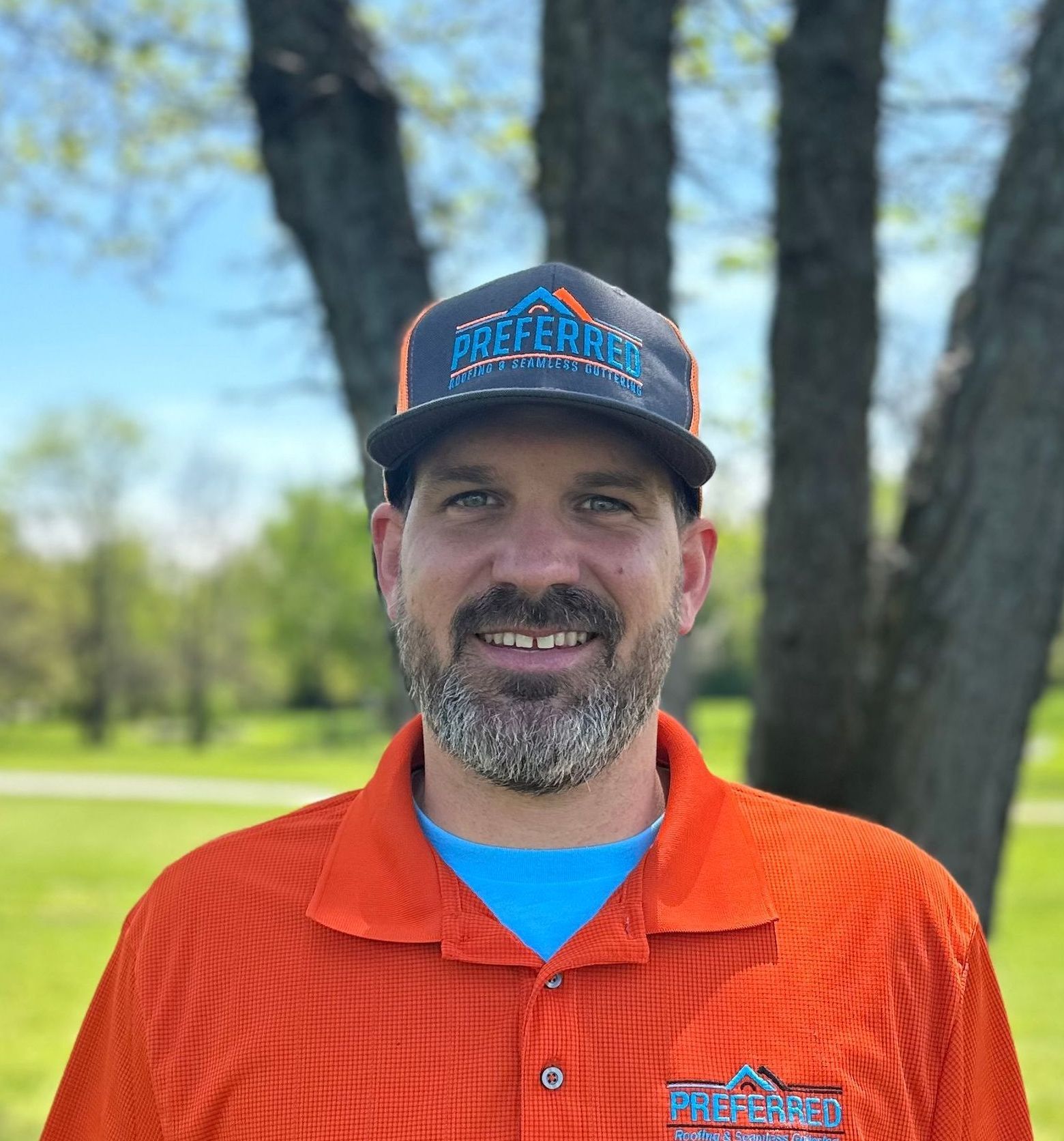 A man with a beard is wearing an orange shirt and a baseball cap.