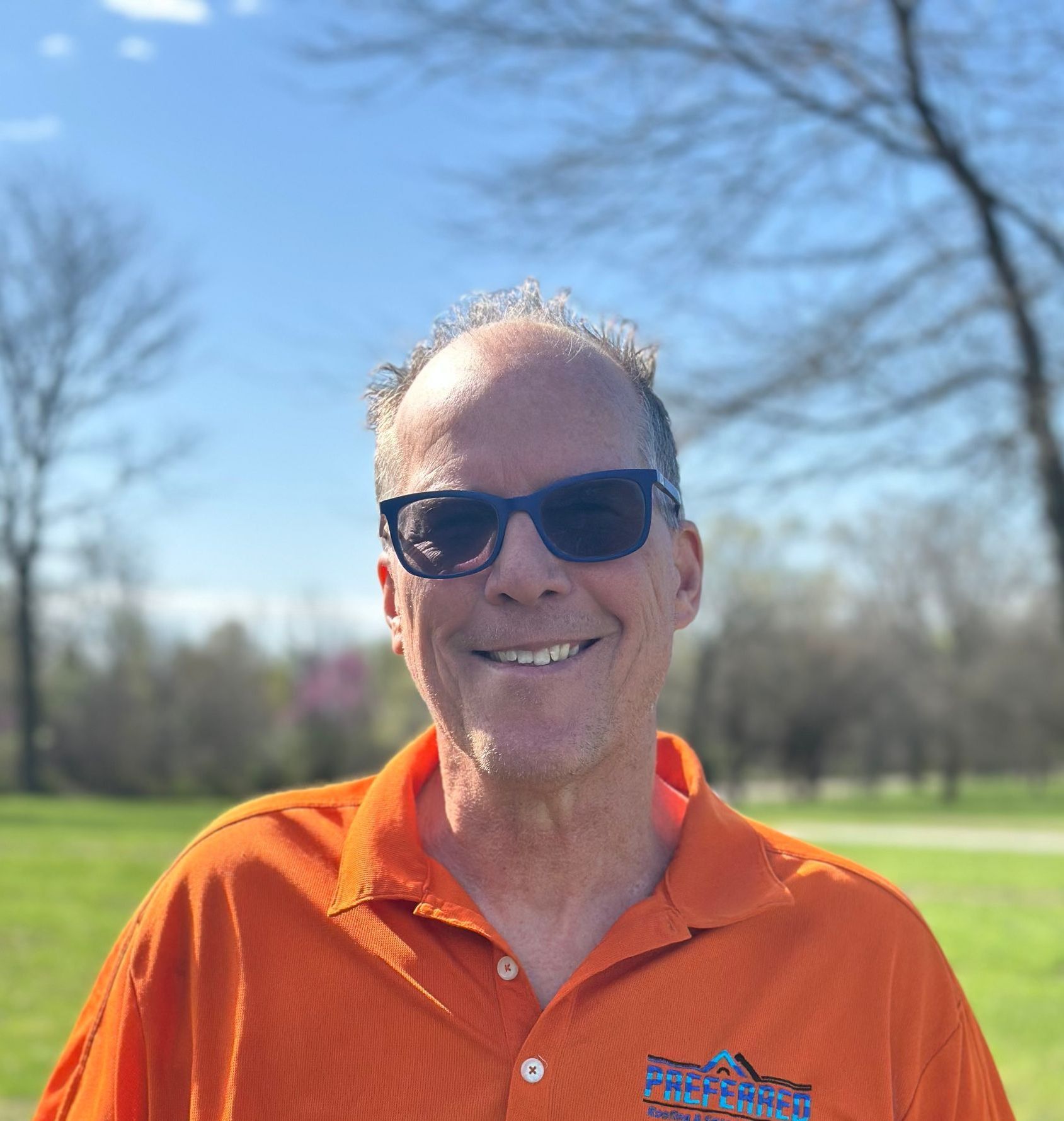 A man wearing sunglasses and an orange shirt is smiling for the camera