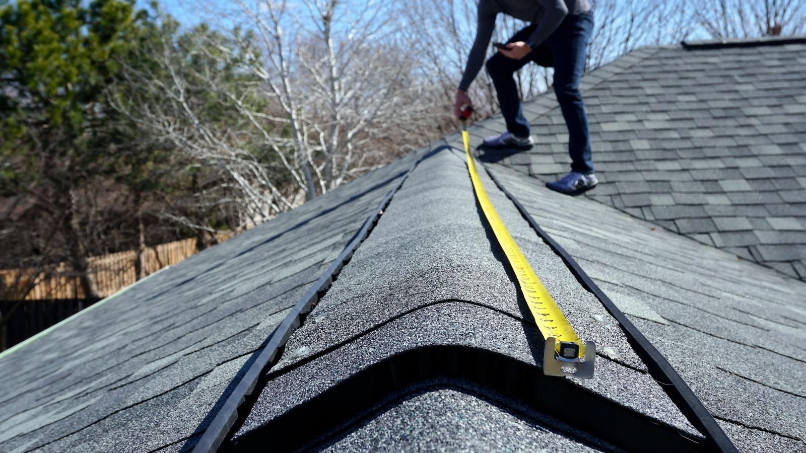 A man is measuring a roof with a tape measure.