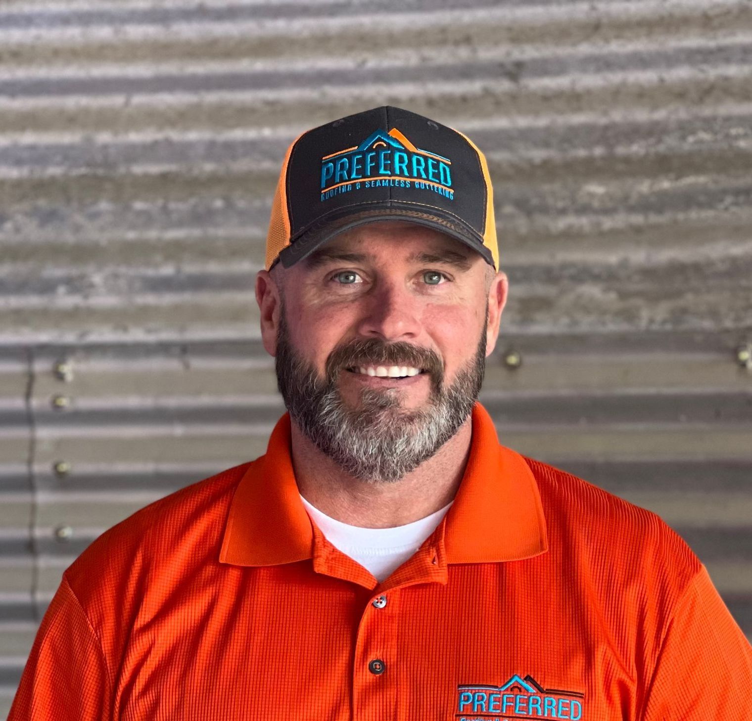 A man with a beard is wearing a hat and an orange shirt.