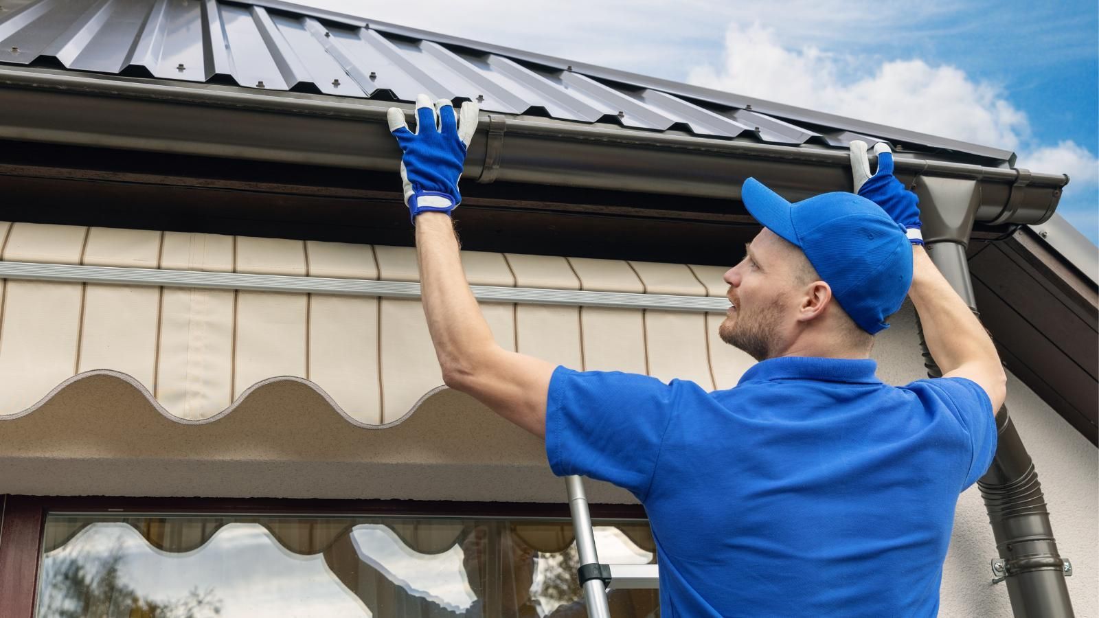 A man is installing a gutter on the side of a house.