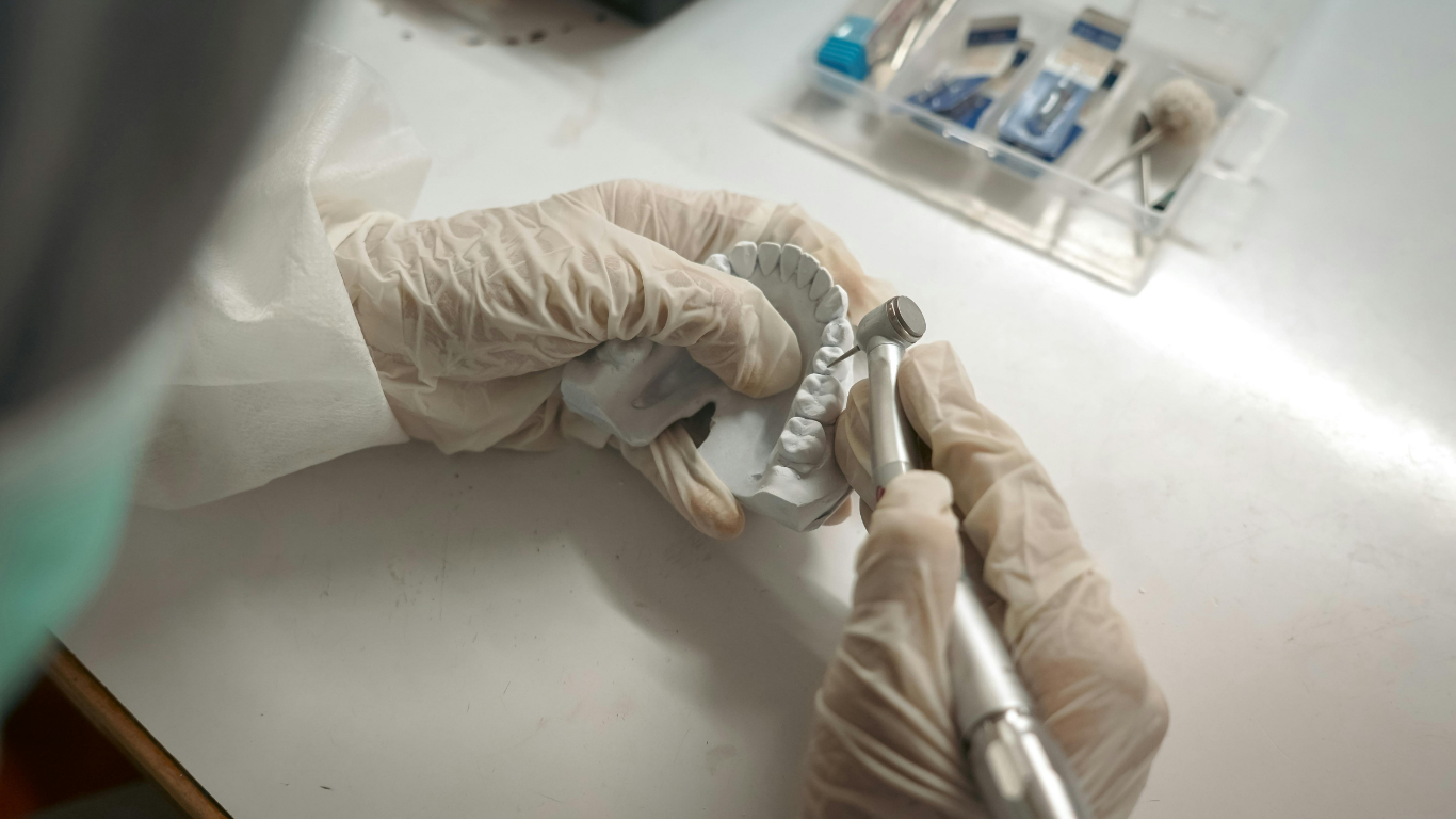 Person in gloves uses a dental drill on a dental mold.
