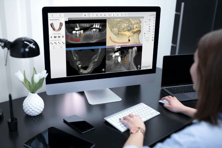 Woman using computer displaying dental X-ray images, assessing patient's oral health in a medical office.
