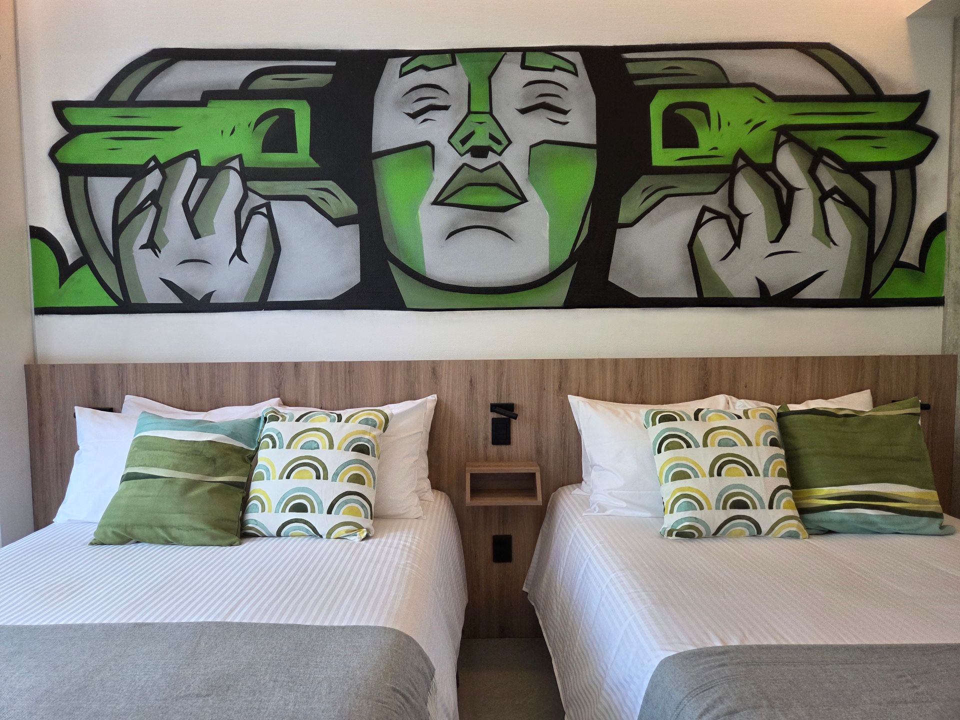 Two twin beds with green pillows and a mural of a face with green accents above.