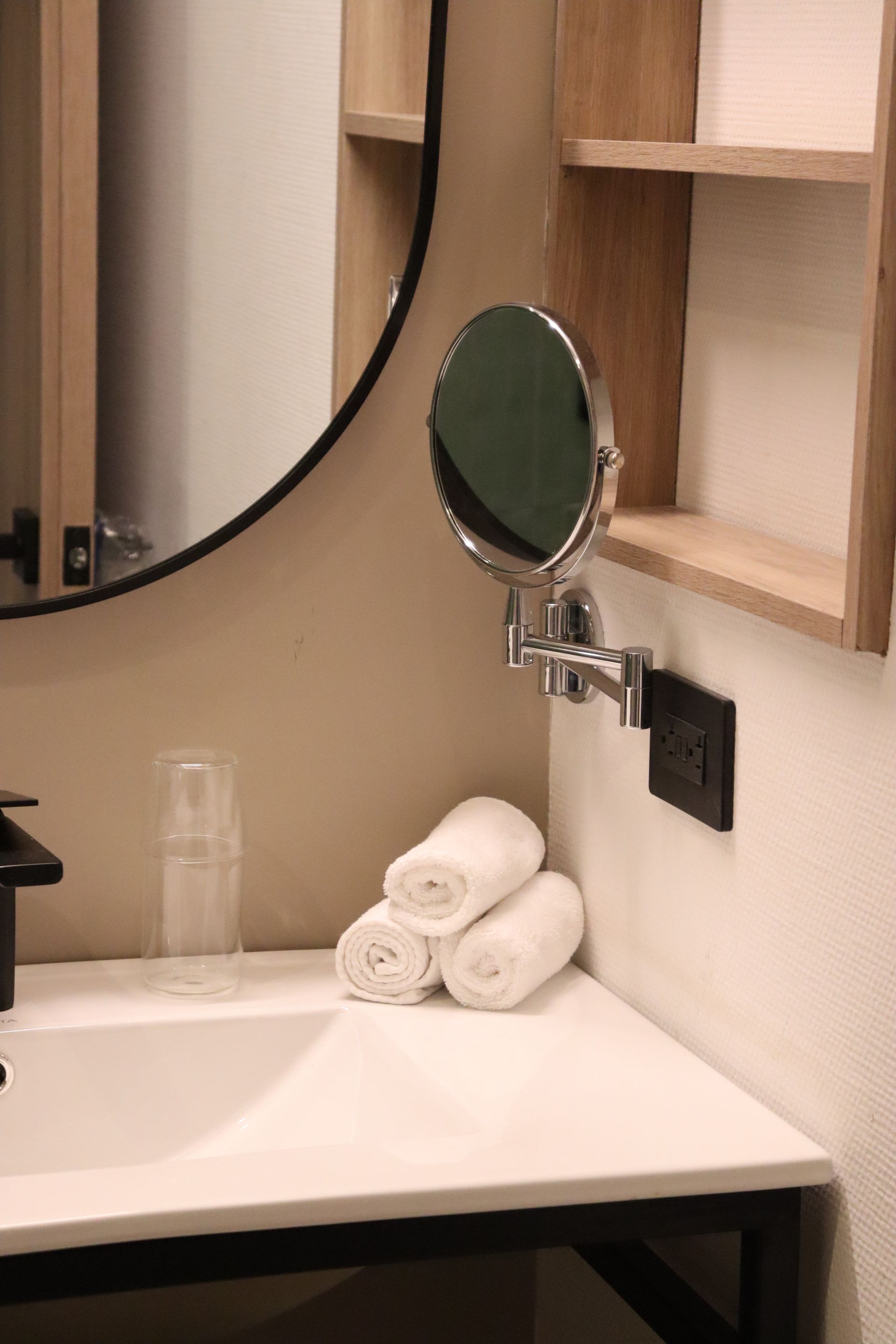 Bathroom sink with towels, a magnifying mirror, and a large round mirror.