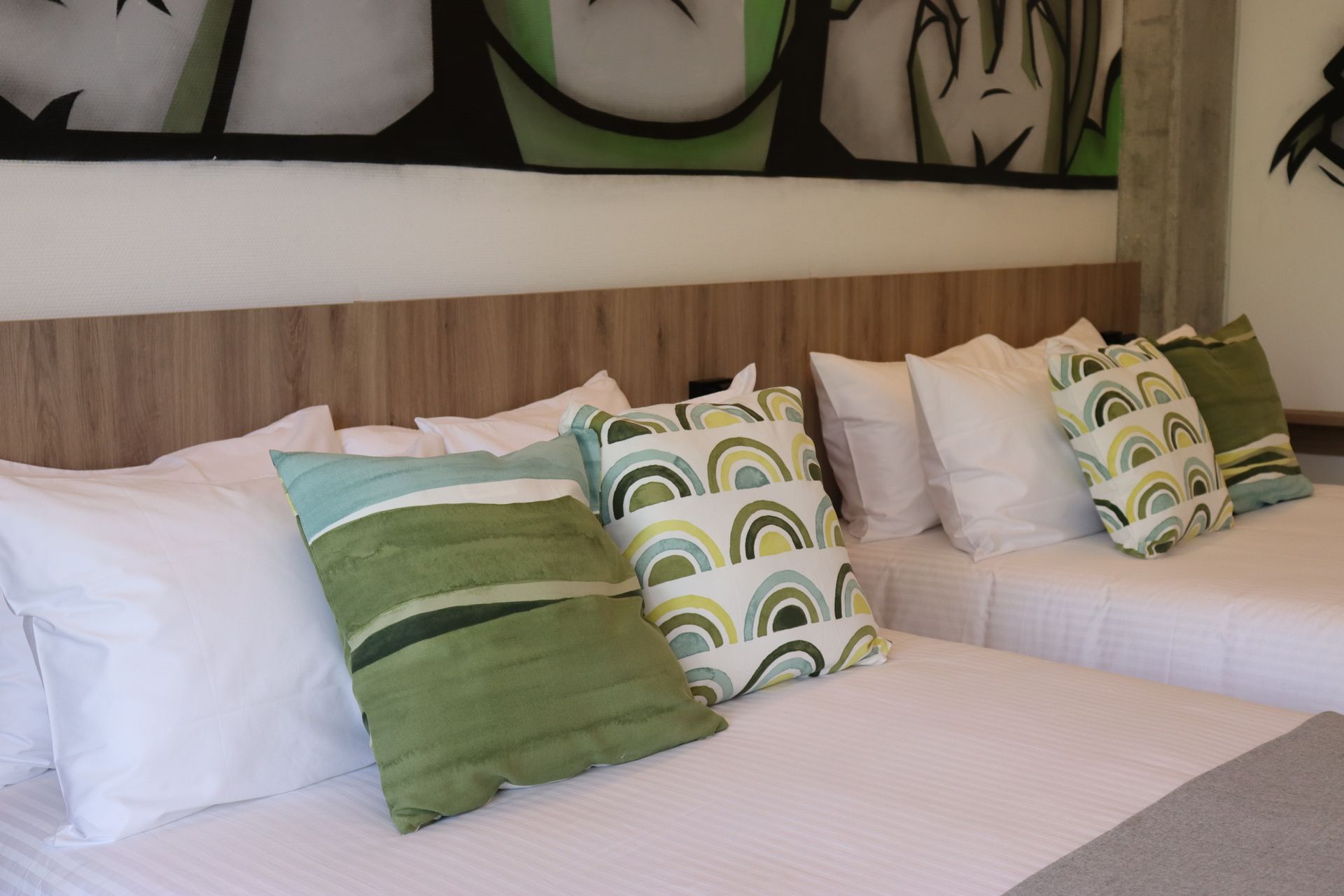 Two beds with white bedding and decorative green pillows under artwork.