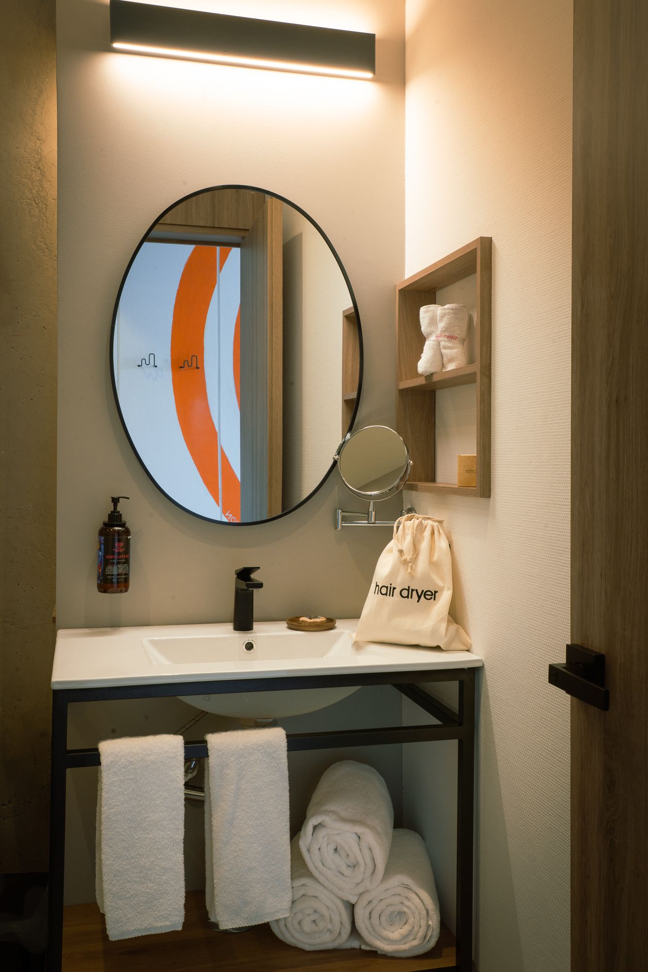 Bathroom with a round mirror, sink, and towels. A shelf holds towels and toiletries.