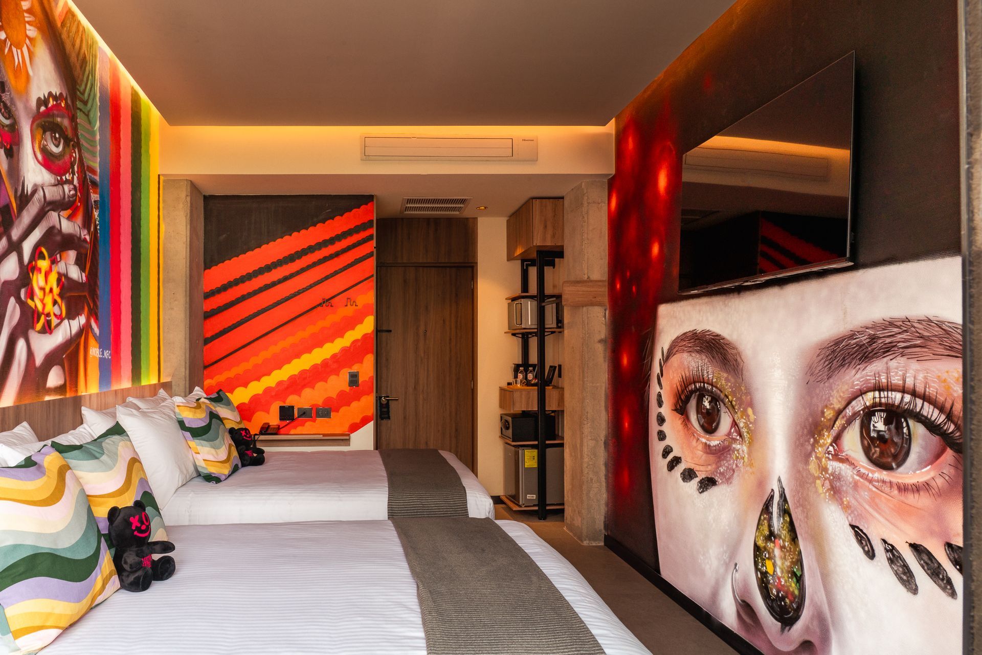 A hotel room with colorful artwork, a large bed, and a wall-mounted TV.