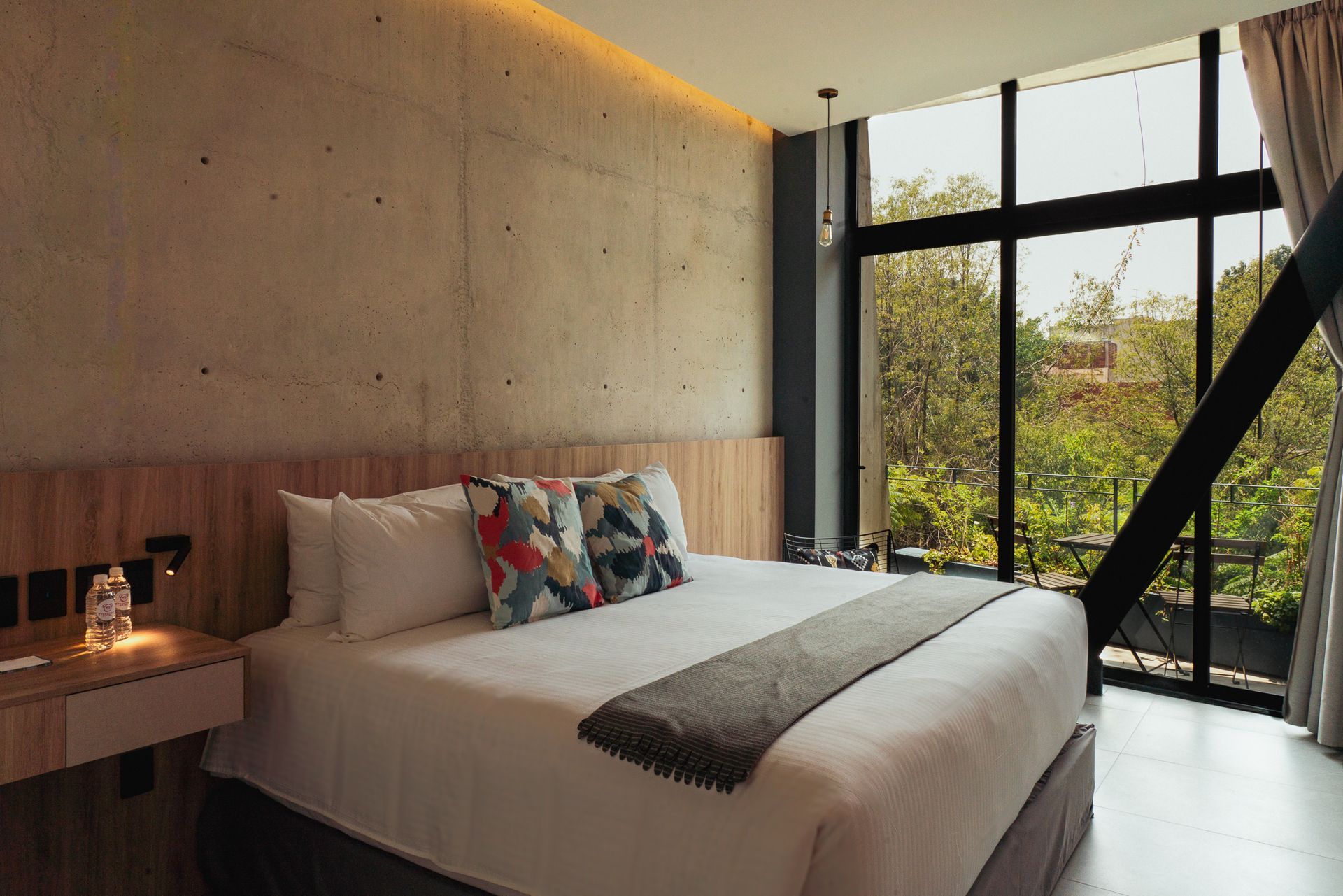 Bedroom with a large bed, concrete wall, and floor-to-ceiling windows overlooking greenery.