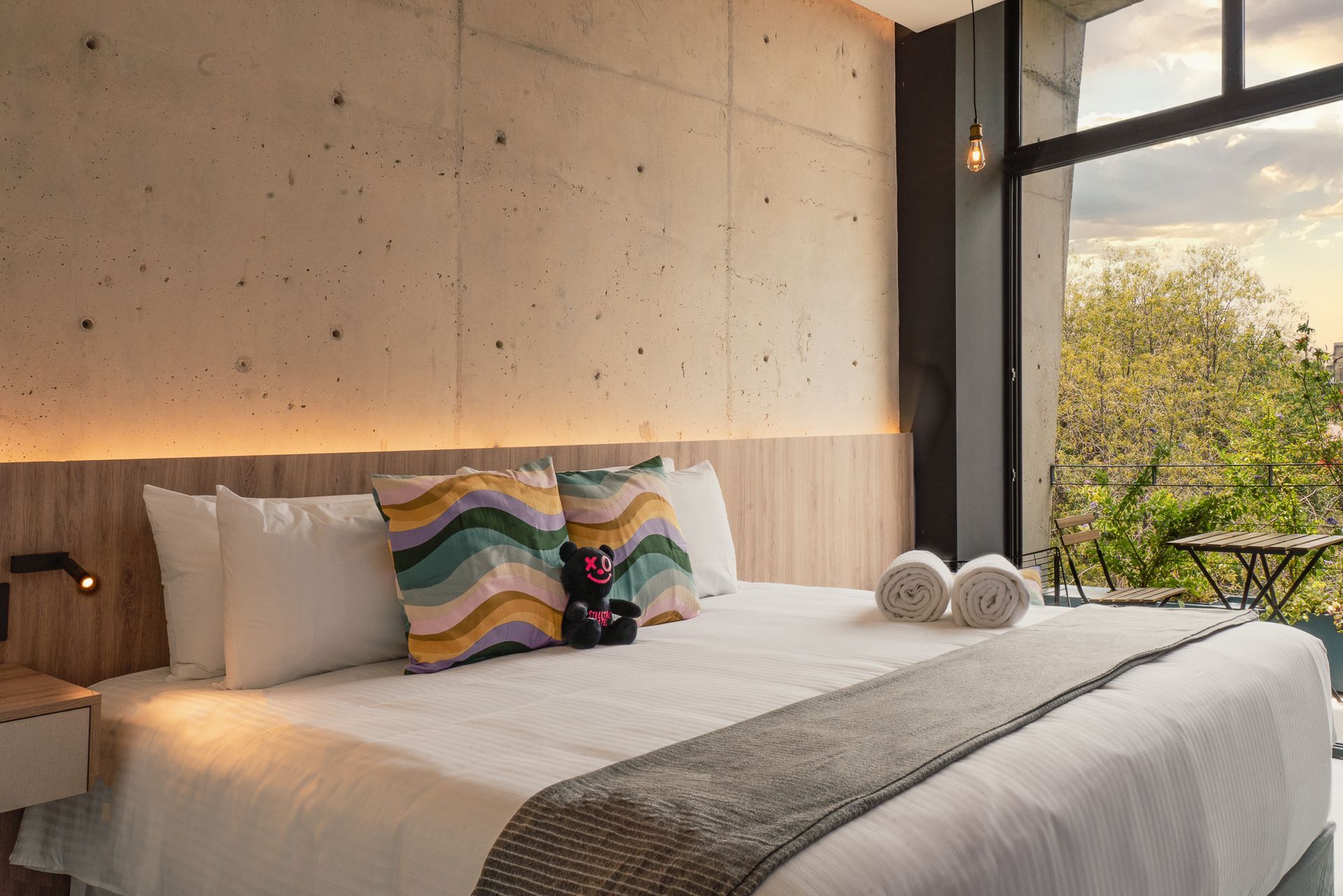 Bedroom with king-sized bed, decorative pillows, towels, and large window overlooking trees.