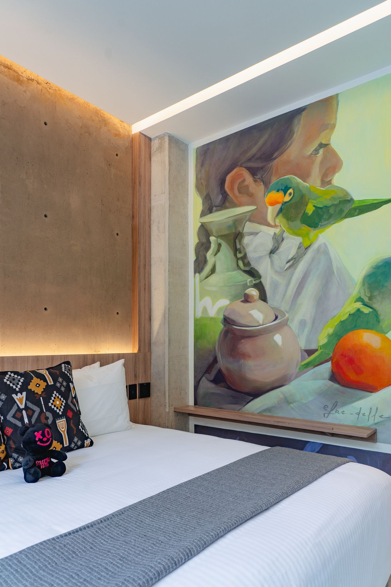 Bedroom with mural, bed, pillows, and decorative shelf. The mural depicts a person with birds and food items.