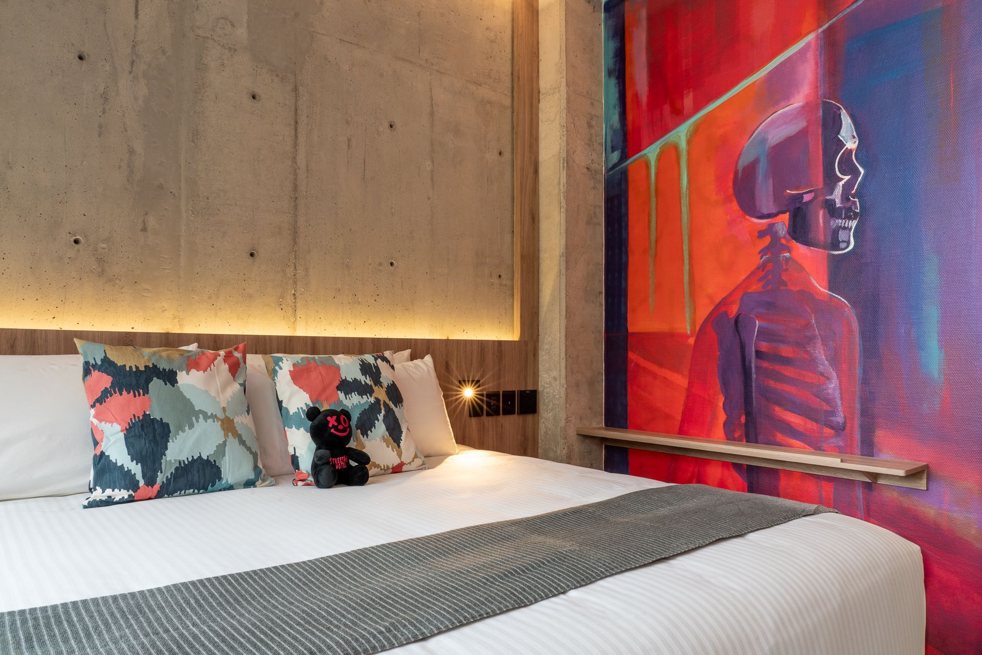 Bedroom with white bed, colorful pillows, and graffiti art on a concrete wall.